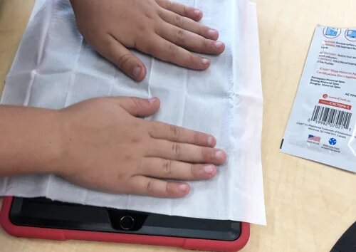 A teacher and students using iCloth wipes to clean a classroom set of 25 iPads. 